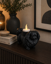 Matte zwarte Pekingees hond waxinelichthouder met LED-waxinelichtje op donker houten kastje met sfeervolle decoratie langs de wand.