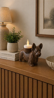 Bruine Skye Terrier hond waxinelichthouder op houten kast in warme huiselijke woonkamer setting.