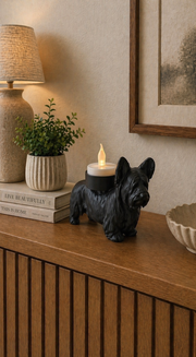 Zwarte Skye Terrier hond waxinelichthouder op houten kast met warme verlichting in modern interieur.