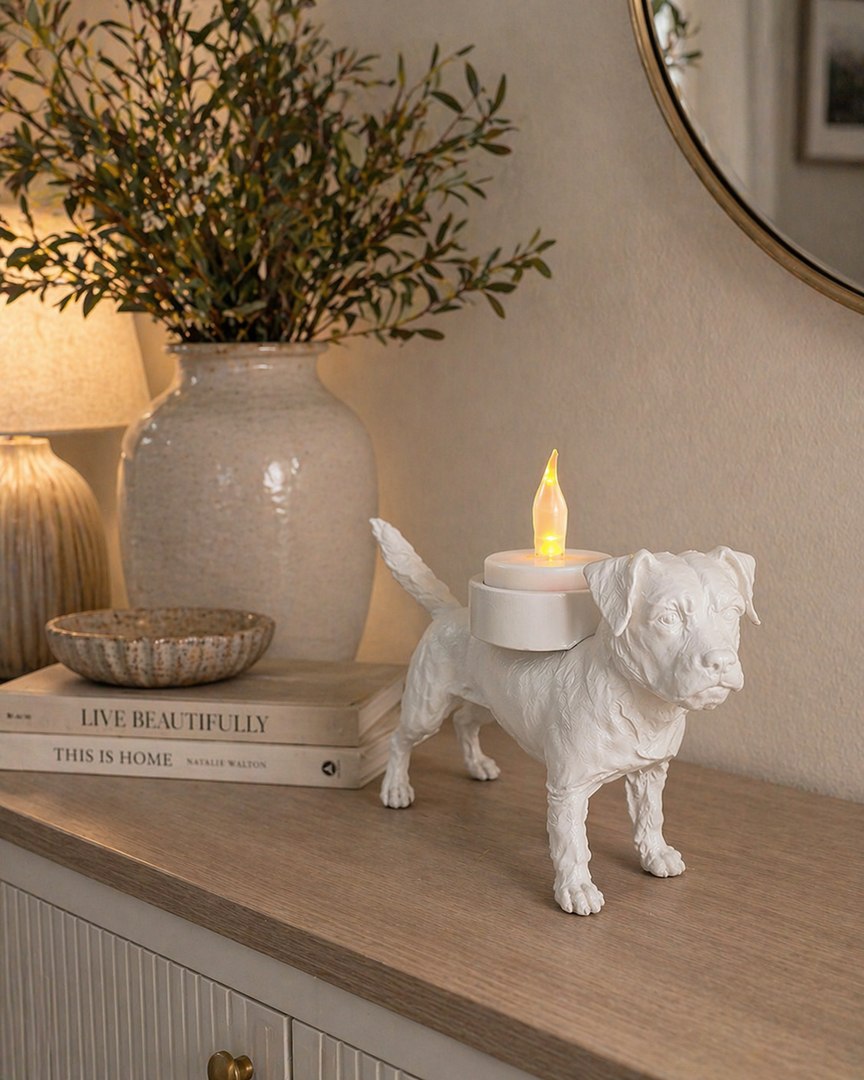 Witte Waxinelichthouder Border Terrier met led-waxinelichtje op een kastje langs de muur in stijlvolle huiselijke setting met vaas en lamp.