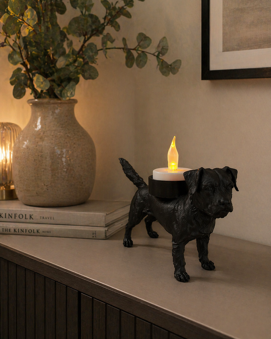 Zwarte Waxinelichthouder Border Terrier met led-waxinelichtje op een kastje langs de wand in moderne warme woonomgeving met decoratieve accessoires.