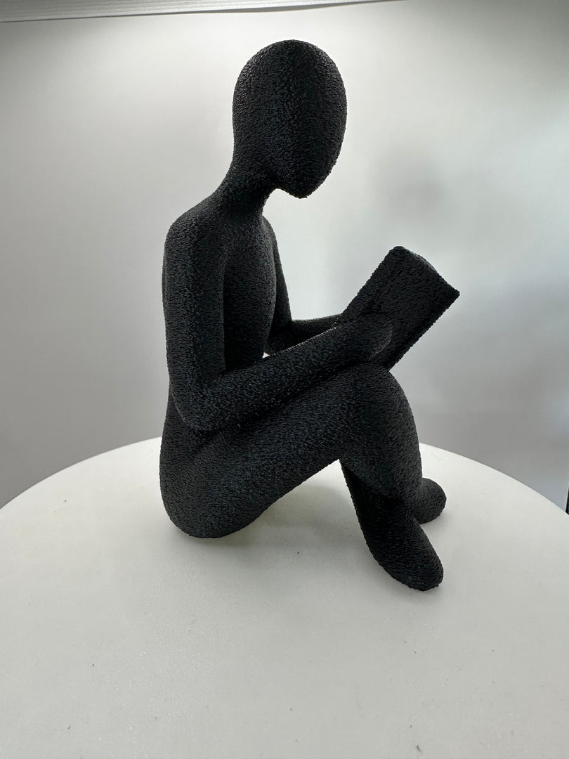 Modern decoratief beeld van een lezende figuur met boek vanuit rechterzijde gefotografeerd.