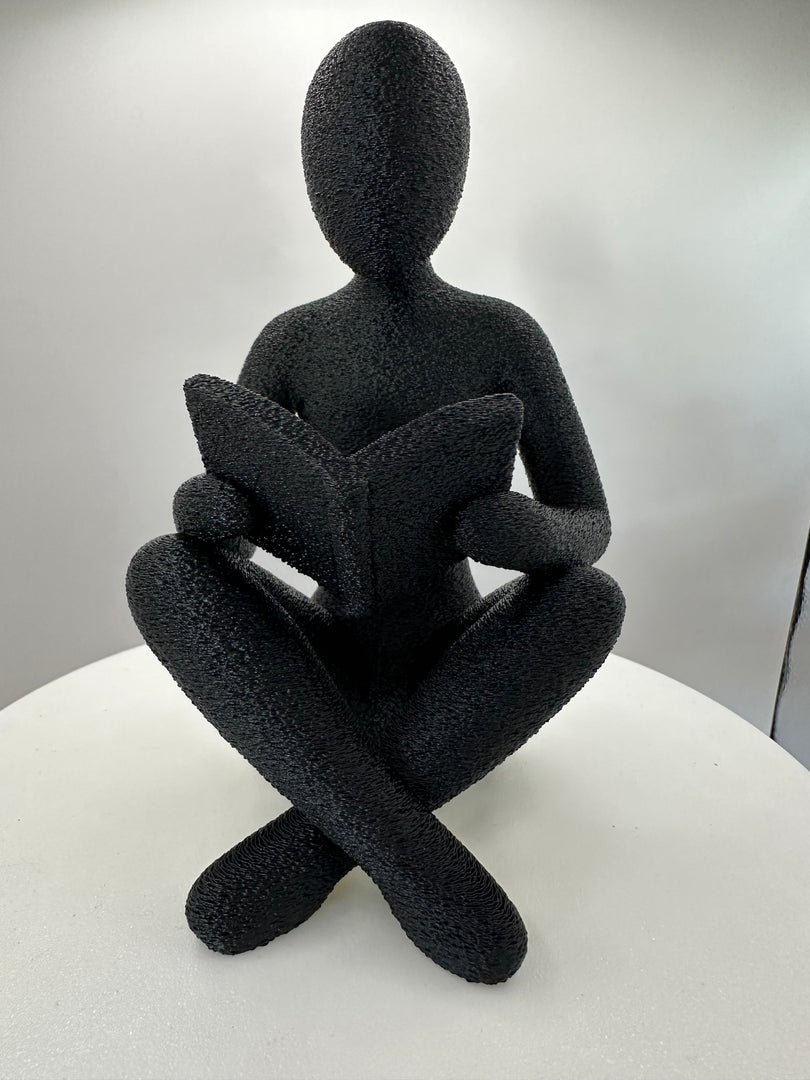 Minimalistische sculptuur van een lezende figuur met boek gezien vanuit voorkant