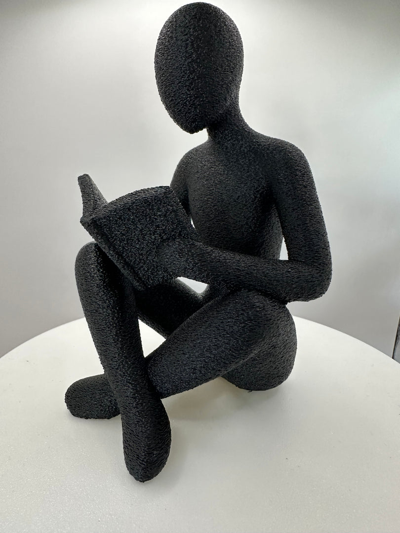 Minimalistische sculptuur van een lezende figuur met boek gezien vanuit zijprofiel
