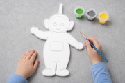 Kind schildert een verfbaar Dipsy figuur uit de Teletubbies met meegeleverde verf in groen, grijs en geel en een penseel van Hunoba Creative.