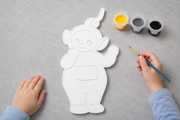 Kind schildert een verfbaar Laa-Laa figuur uit de Teletubbies met meegeleverde verf in geel, grijs en zwart en een penseel van Hunoba Creative.