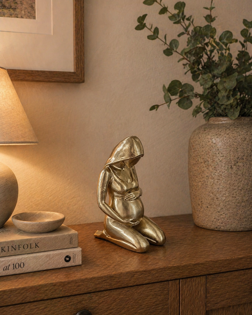 Goudkleurig zwanger vrouw beeld als modern sculptuur ornament op houten kastje in warme huiselijke setting, stijlvolle woondecoratie voor mama.