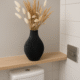 Zwarte siervaas met droogbloemen op een houten wandplank in een modern toilet