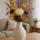 Witte siervaas met bloemen op een ronde houten tafel in een lichte woonkamer