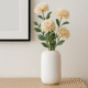 Witte Siervaas Rosella Chic met beige bloemen op een houten dressoir met wanddecoratie erboven.
