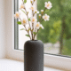 Zwarte Siervaas Rosella Chic met witte hortensia’s op een ronde houten tafel in een lichte kamer.
