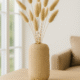 Beige Siervaas Rosella Chic met bunny tails op een houten salontafel voor een lichte bank.